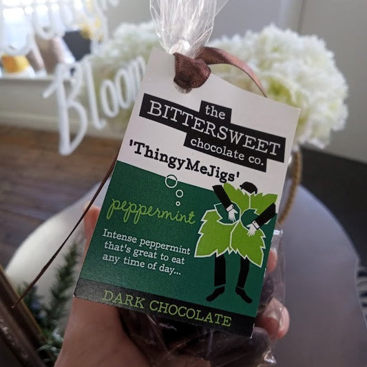 Bag of dark chocolate with a 'Bittersweet Chocolate Co.' tag, held in front of a blurred indoor background.