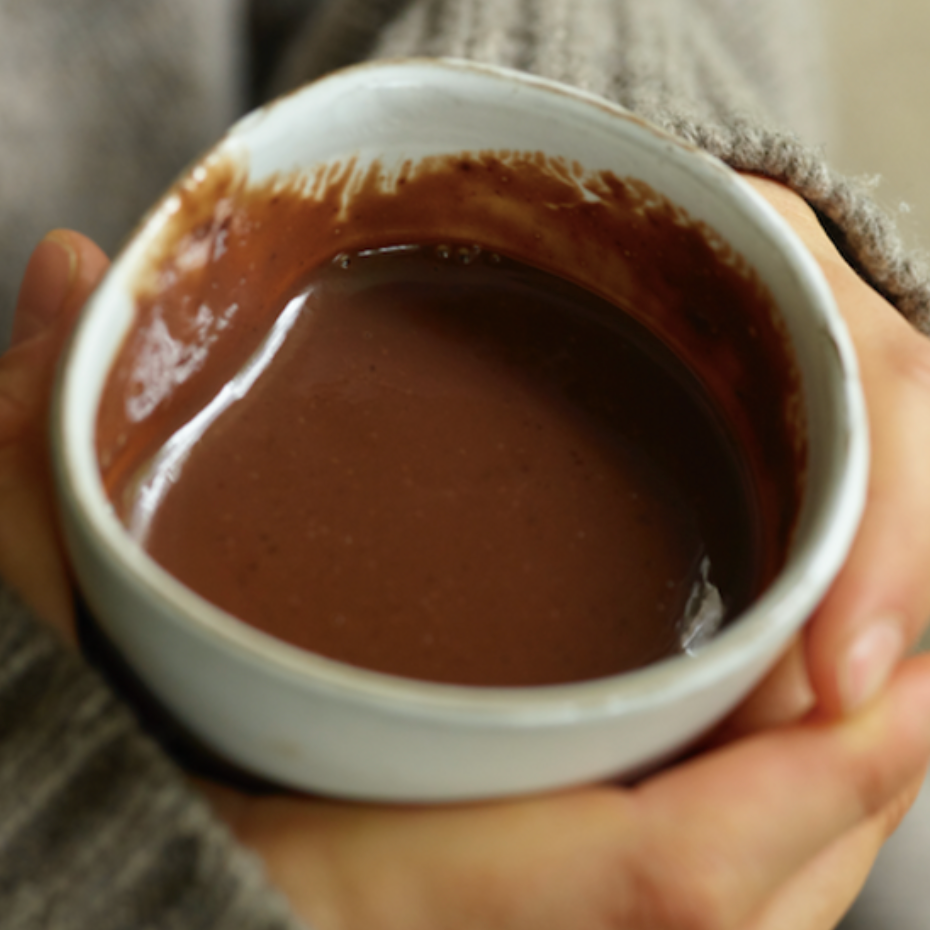 Person holding a small white mug filled with hot chocolate.