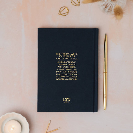 dark blue journal with gold text and a gold pen on a light pink surface