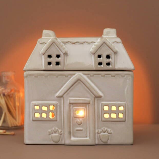 Ceramic house-shaped lantern with a warm glow on a brown background