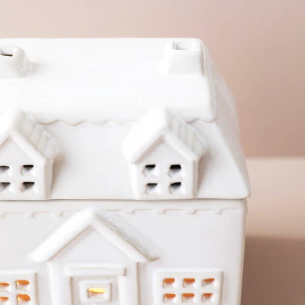 White ceramic house-shaped lantern with small windows on a light pink background