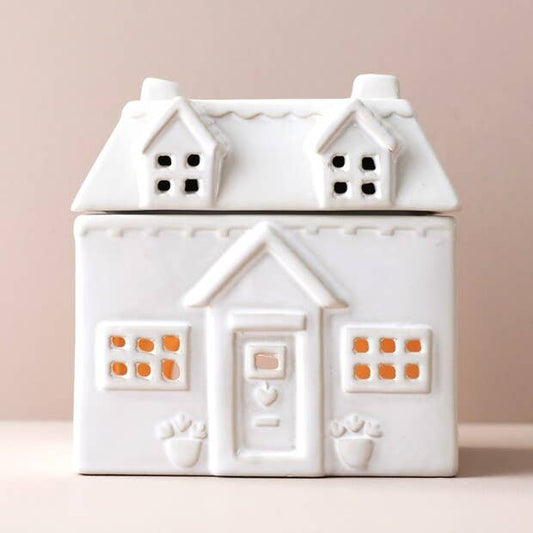 White ceramic house-shaped wax burner on a pink background