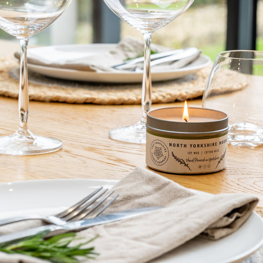 Candle in a decorative tin on a table setting with wine glasses and plates.