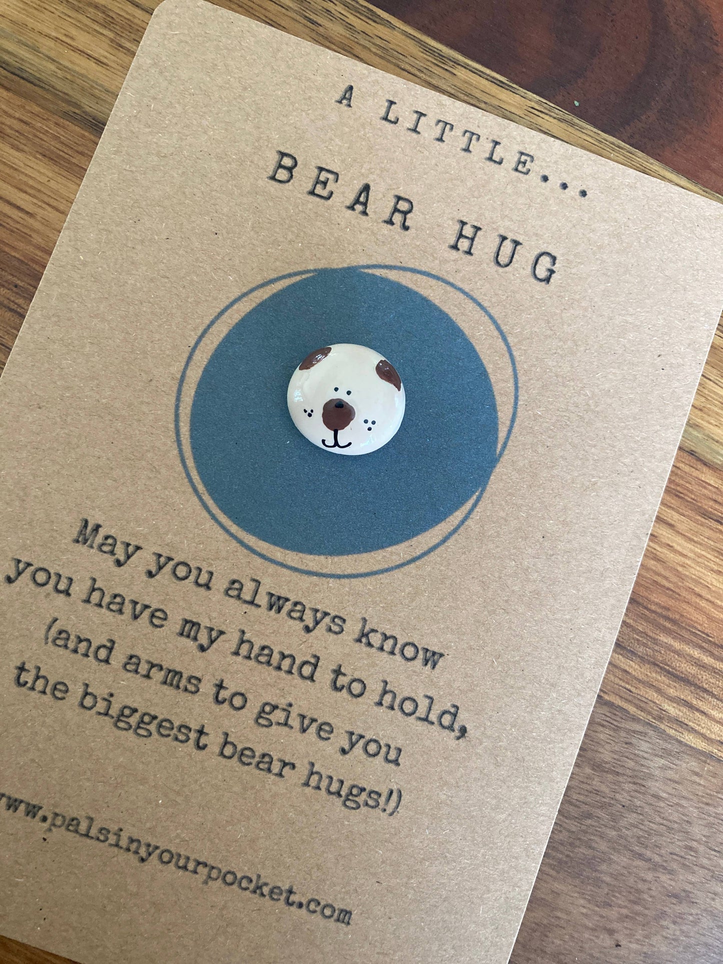Card with a bear pebble and text on a wooden surface