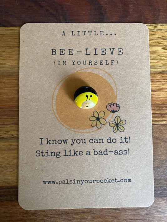 Token with bee design on a kraft paper card with motivational text, placed on a wooden surface.