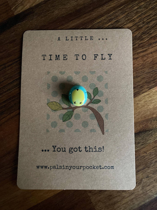 Token with a bird design on a card that says 'A little time to fly, you got this!' on a wooden surface.