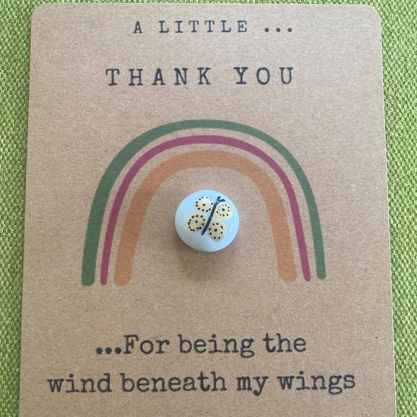 Card with rainbow design and charm, featuring text 'A little thank you for being the wind beneath my wings' on a green background.