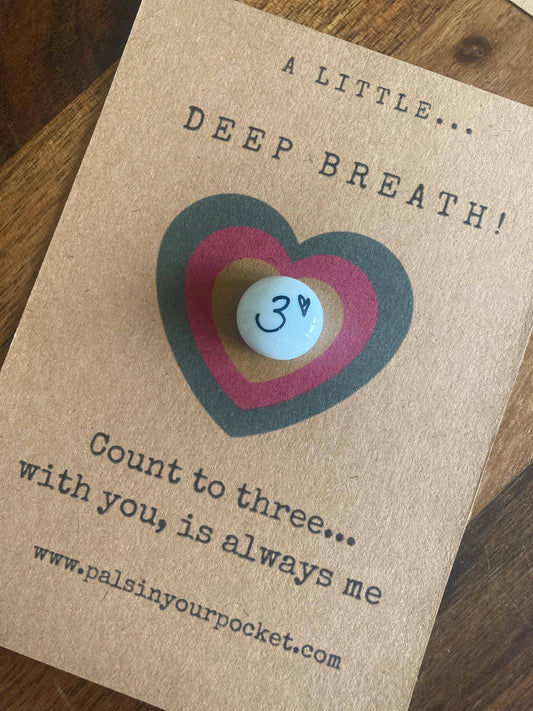 Kraft paper card with a heart design and a small token, on a wooden surface.