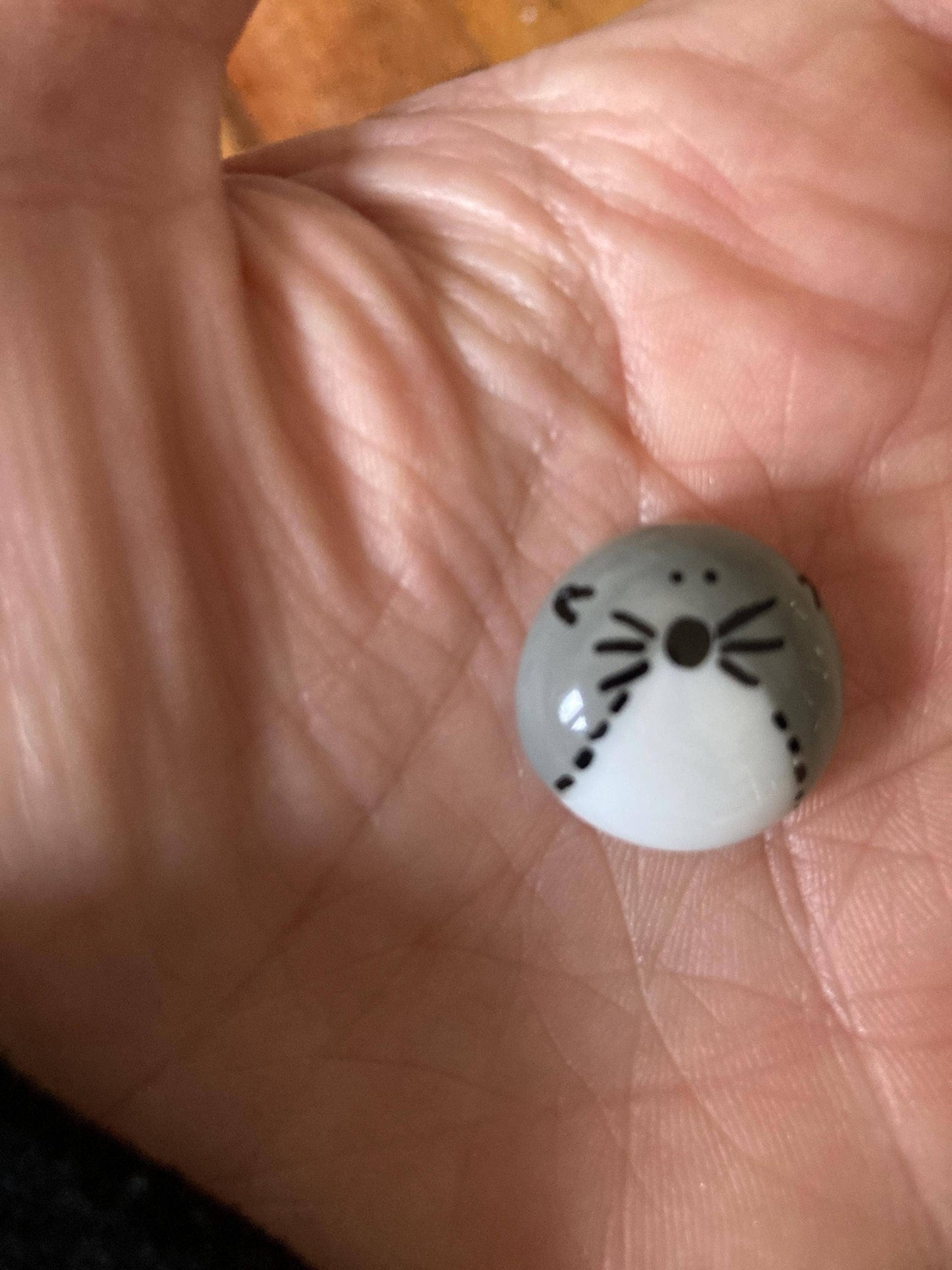 Small round fused glass token with otter face design held between fingers