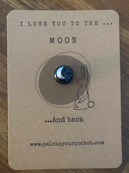 Token with moon design on a card with text 'I love you to the moon and back' on a wooden surface.