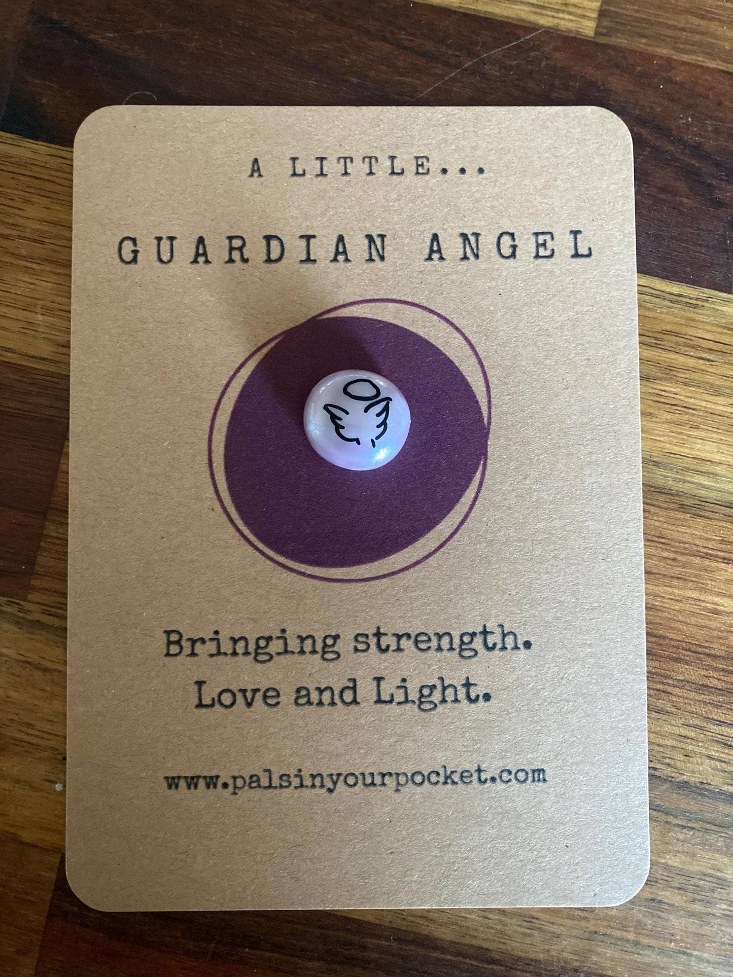 Guardian angel charm on a brown card with text on a wooden surface