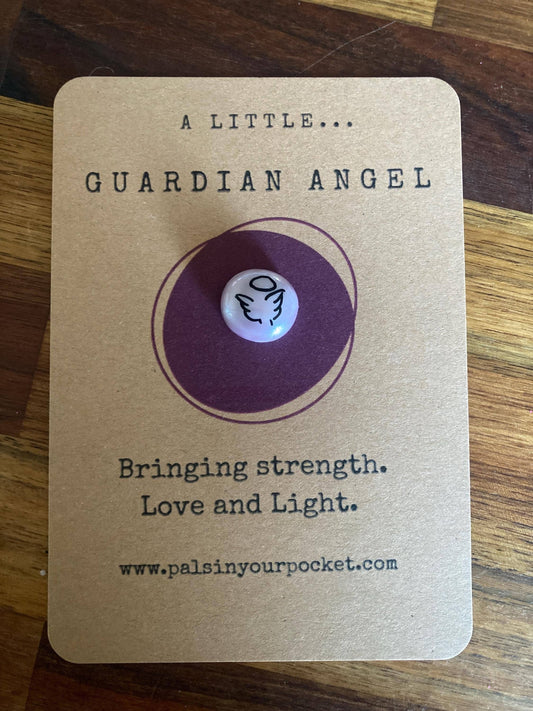 Guardian angel charm on a brown card with text on a wooden surface
