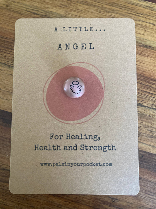 Small angel charm on a card with text about healing, health, and strength on a wooden surface.