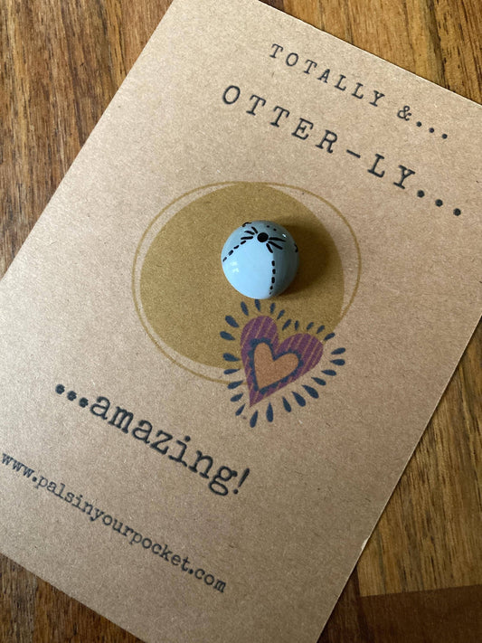 Otter pebble with heart design on a brown card with text