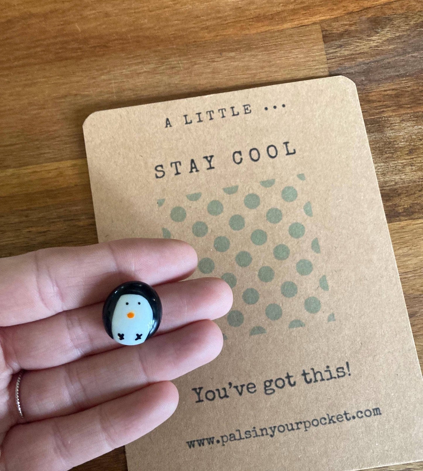 Penguin charm held by a hand on a 'Stay Cool' card with polka dots