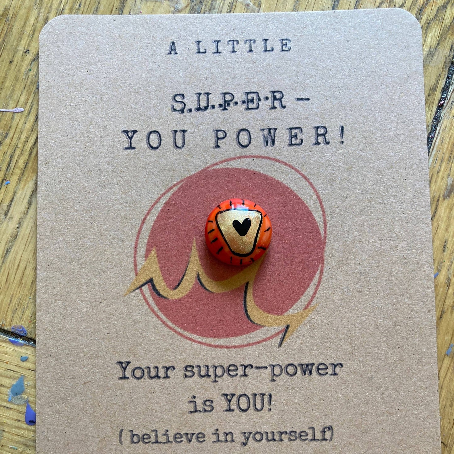 Card with a small red and gold pebble on a textured surface