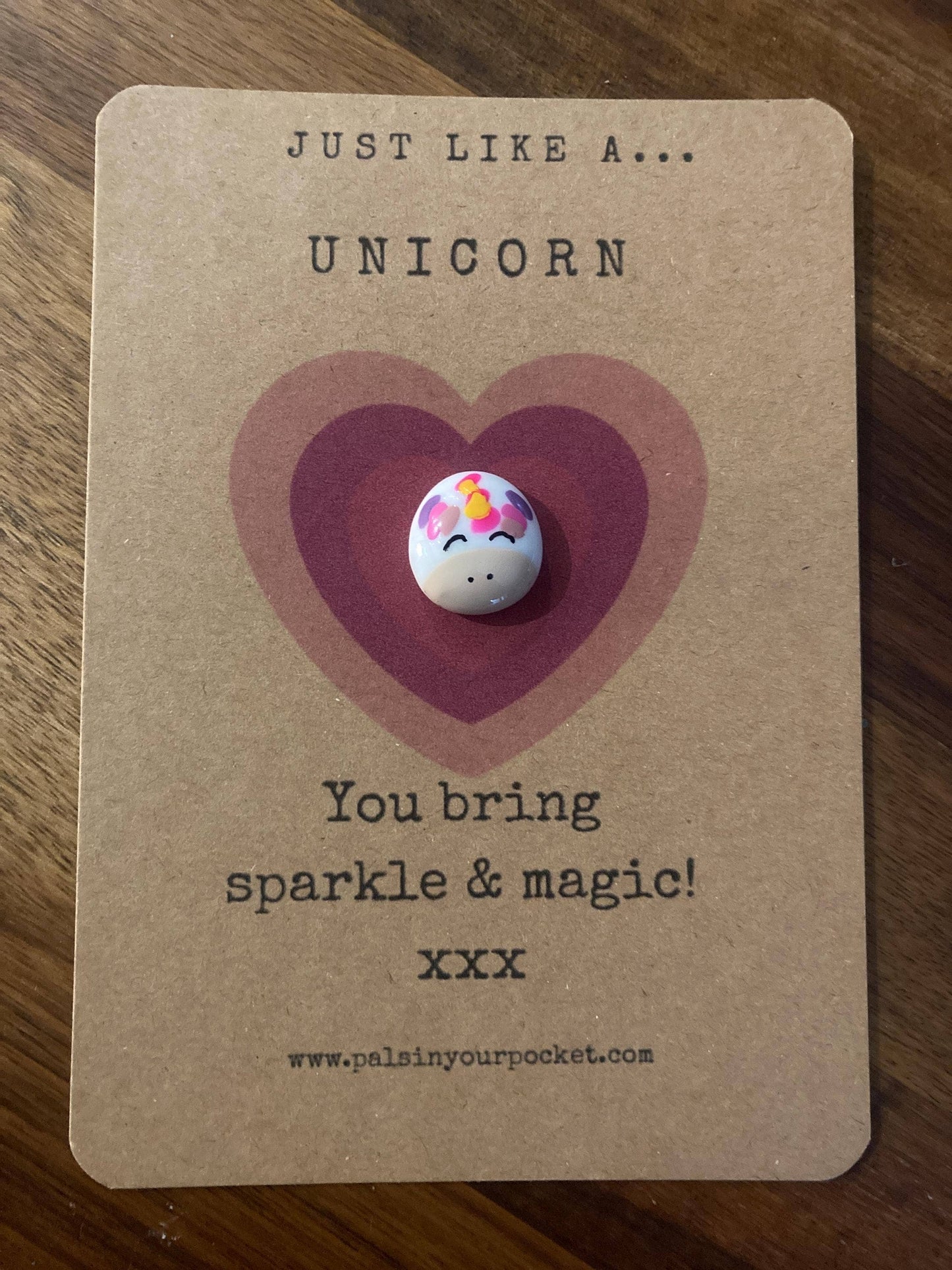 Unicorn-shaped charm on a brown card with text and a heart design