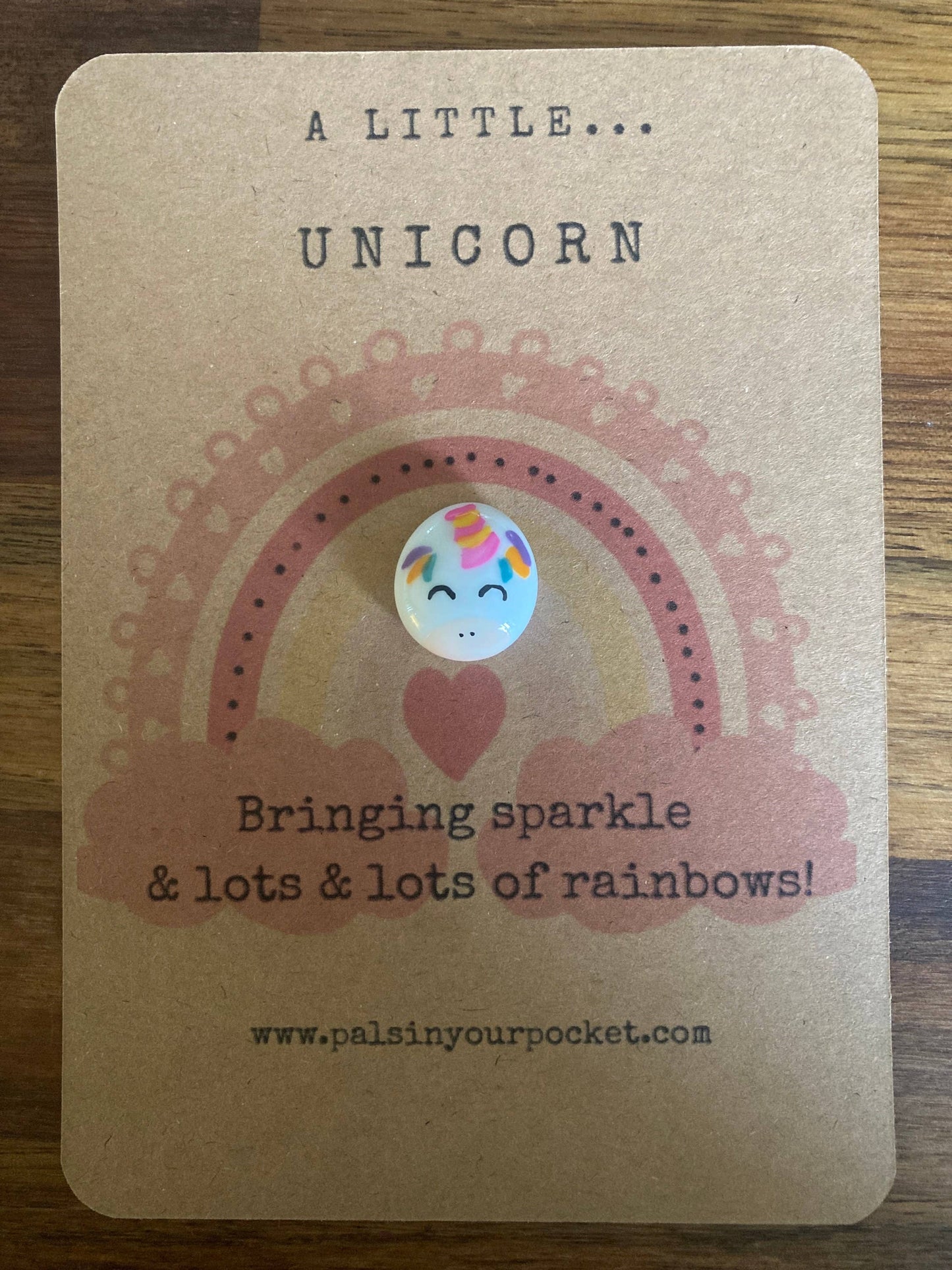 Card with a unicorn button and rainbow design on a wooden surface