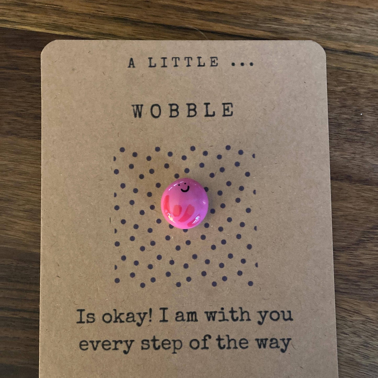 Pink charm on a brown card with text