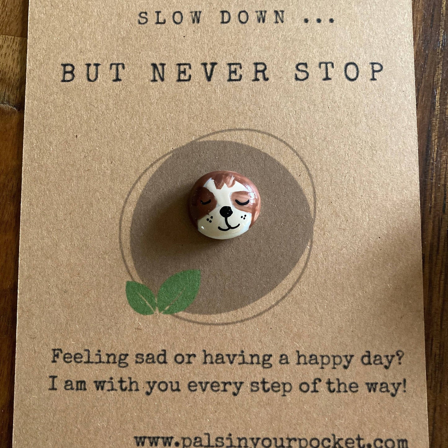 Card with a small sloth figurine and motivational text on a wooden surface
