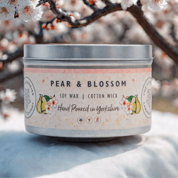 Candle in a tin with 'Pear & Blossom' label against a cherry blossom background