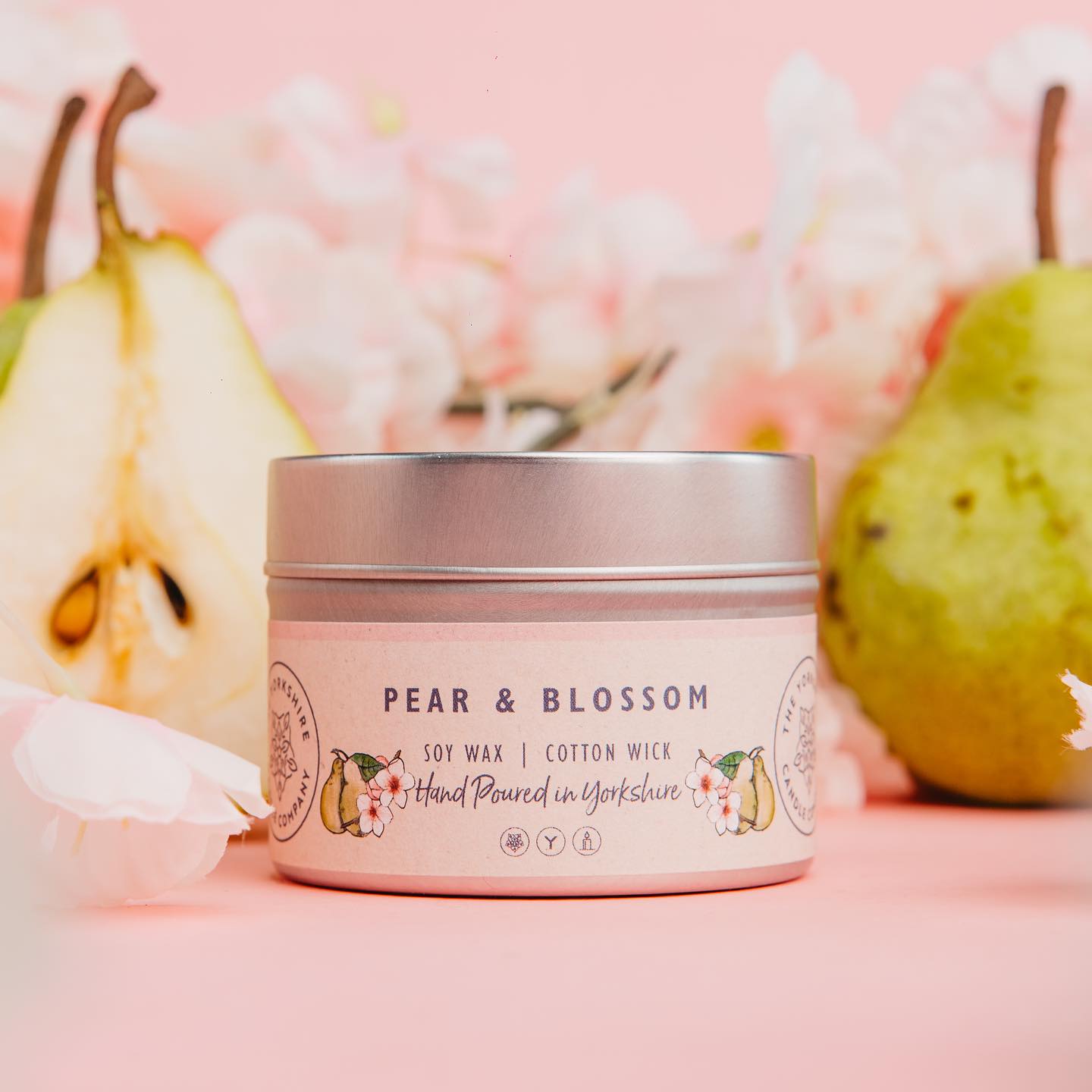 Candle jar labeled 'Pear & Blossom' with pears and flowers on a pink background
