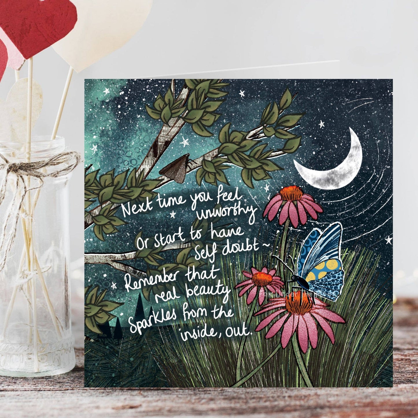 Greeting card with nature-themed design, flowers, and a butterfly on a wooden surface.