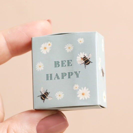 Small box with 'BEE HAPPY' text and bee illustrations held by a hand on a beige background