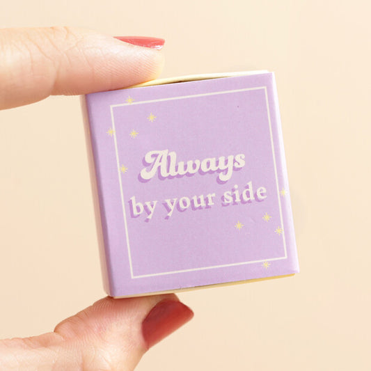 Small purple box with 'Always by your side' text held by a hand on a beige background