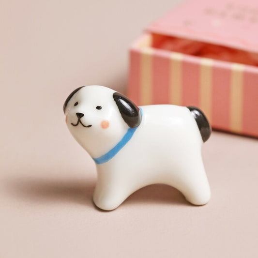 Small ceramic dog figurine with a blue collar on a beige background
