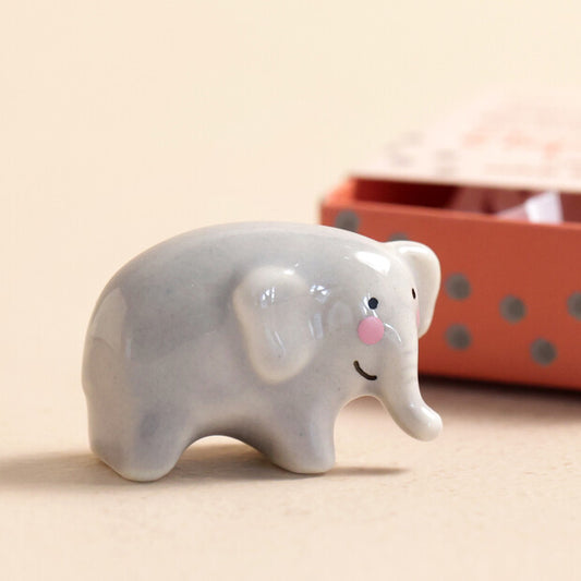 Ceramic elephant figurine with a pink trunk on a beige surface