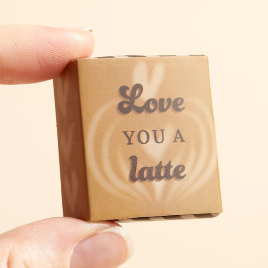 Small brown box with 'Love You a Latte' text held by a hand against a beige background