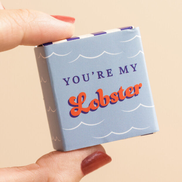 Small blue box with 'You're My Lobster' text held by a hand on a beige background