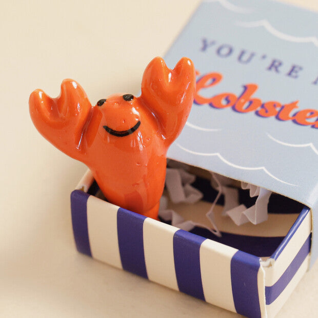 Orange lobster figurine in a striped box with a card in the background