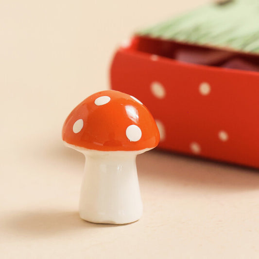 Small ceramic mushroom figurine with a red cap and white spots on a beige background