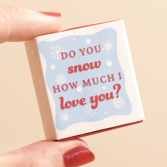 Small box with a snowy design and text held by a hand on a beige background