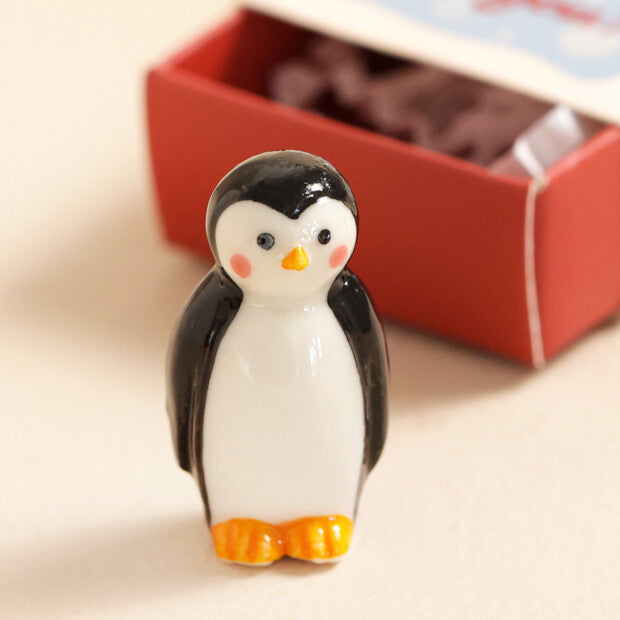 Small penguin figurine on a beige surface with a red box in the background