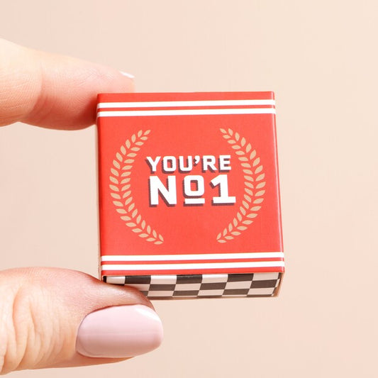 Small red box with 'You're No. 1' text held by a hand on a beige background