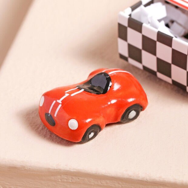 Red car charm on a wooden surface with a checkered box in the background