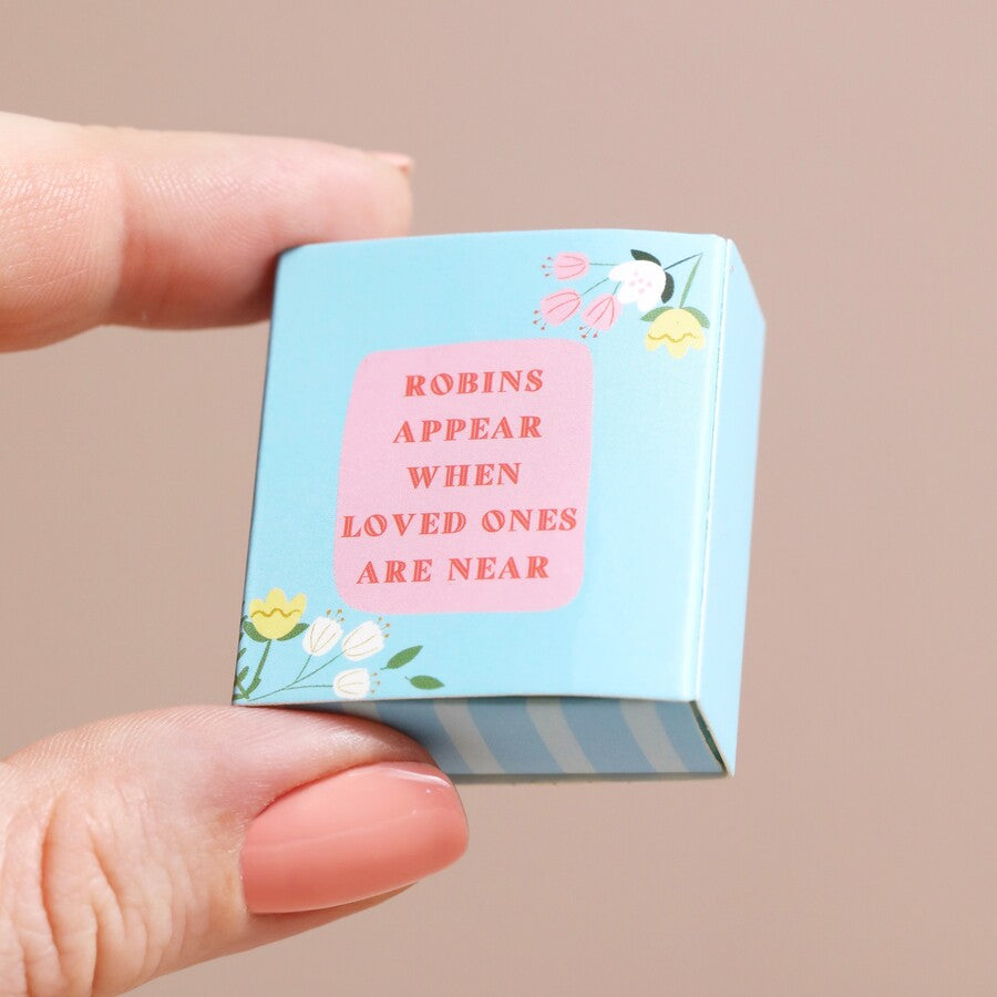 Small blue box with pink text held by a hand against a beige background