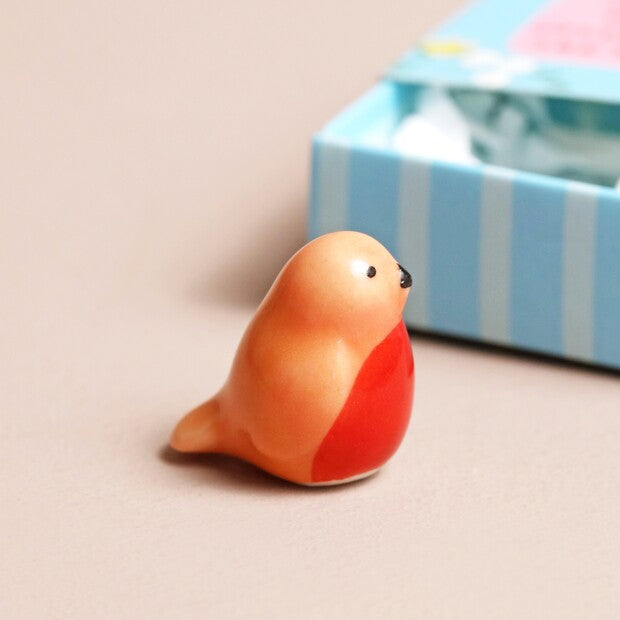 Small ceramic bird figurine on a beige surface with a striped box in the background