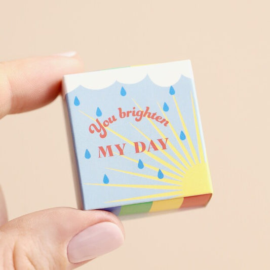 Small box with 'You brighten my day' text held by a hand on a beige background