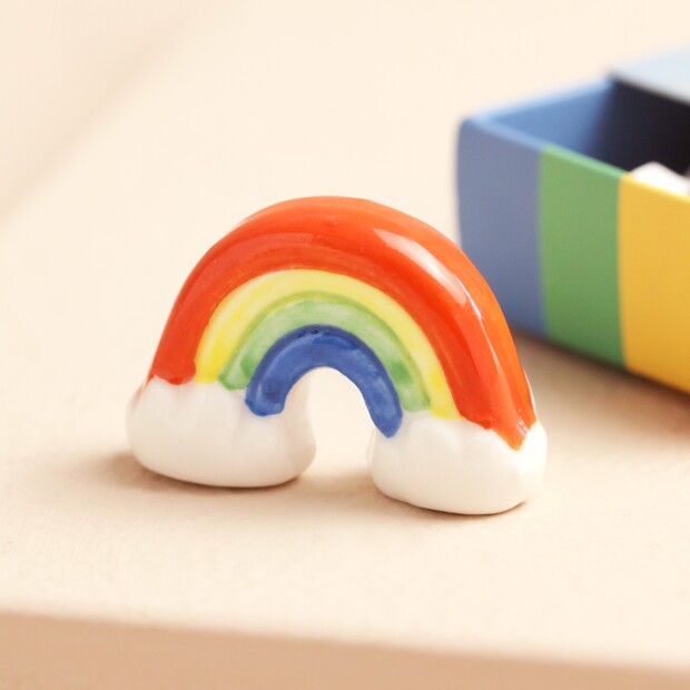 Colorful rainbow-shaped object on a beige surface with a blurred colorful box in the background.