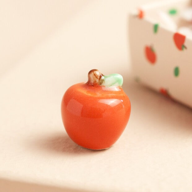 Small ceramic apple figurine on a beige surface with a blurred background