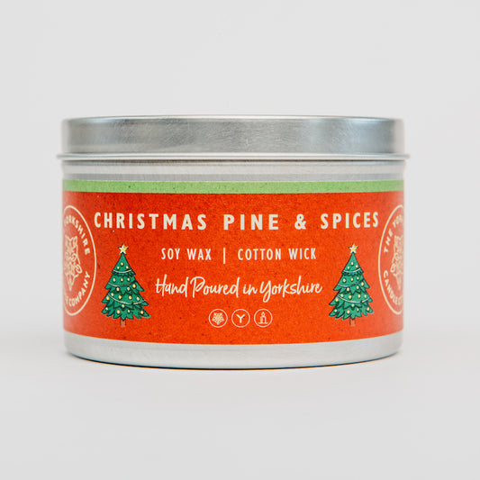 Candle tin labeled 'Christmas Pine & Spices' with a red label and silver lid on a white background.