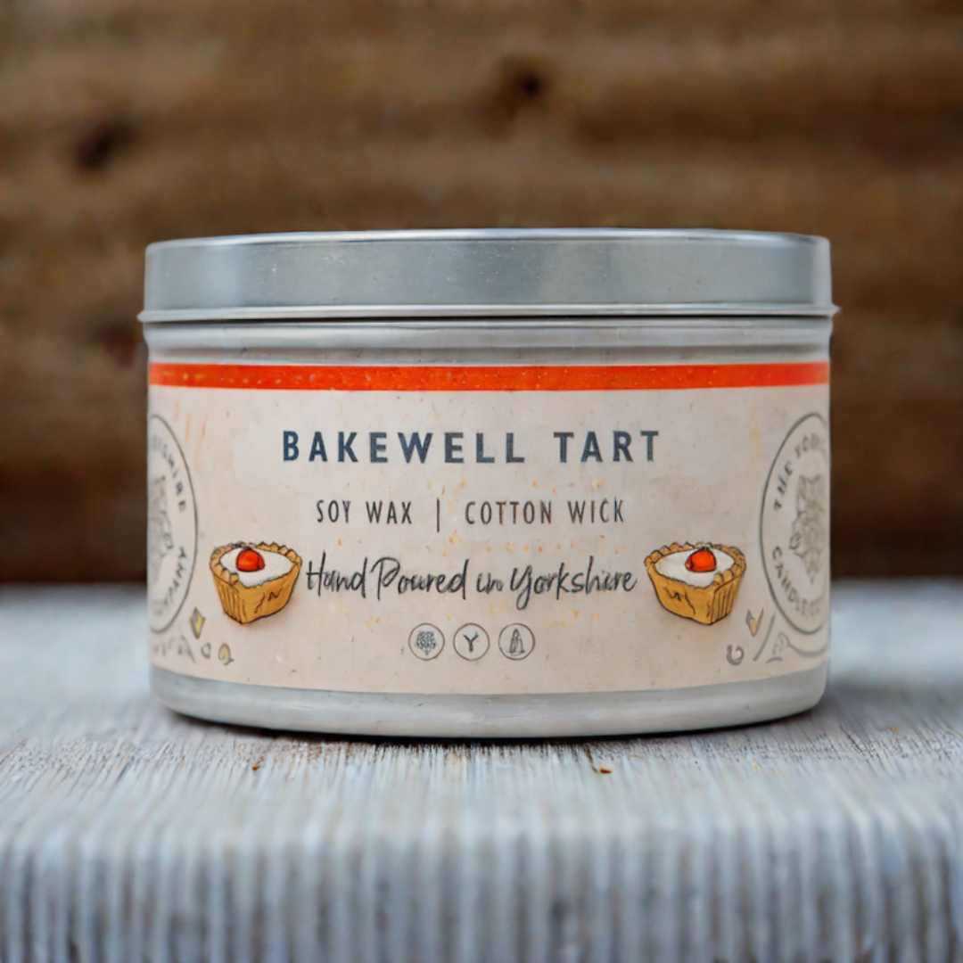 Candle in a tin labeled 'Bakewell Tart' with a rustic background