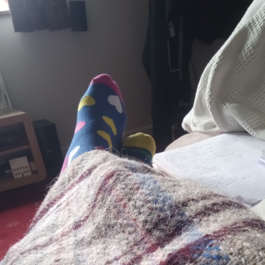A cosy living room corner — the view from the sofa during two weeks of illness in April, bright socks visible as a small reminder that colour still exists.