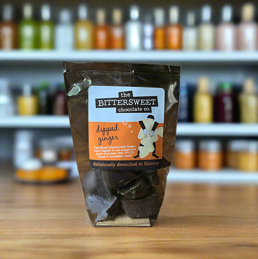 Packaged chocolate dipped ginger on a wooden surface with 'The Bittersweet Chocolate Co.' label.