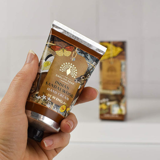 Hand holding a tube of English Soap Company Indian Sandalwood hand cream against a neutral background