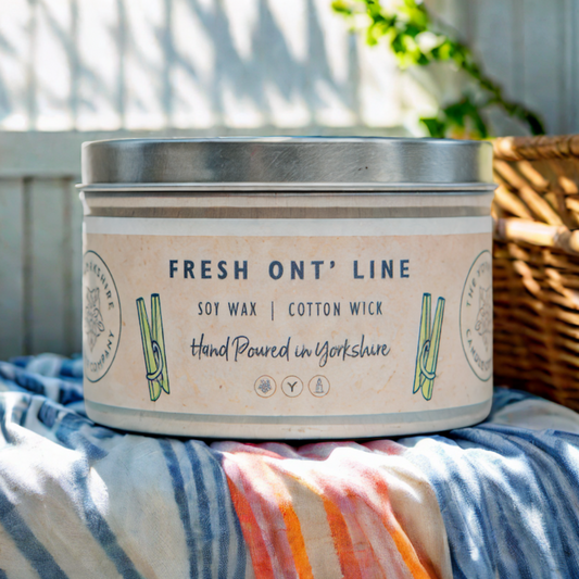 Candle tin labeled 'Fresh Ont' Line' on a striped fabric with a blurred outdoor background